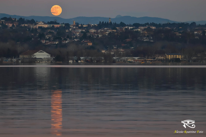 Mentre il sole non è ancora tramontato La luna che sorge da dietro le colline e si specchia nelle acque del lago di Varese